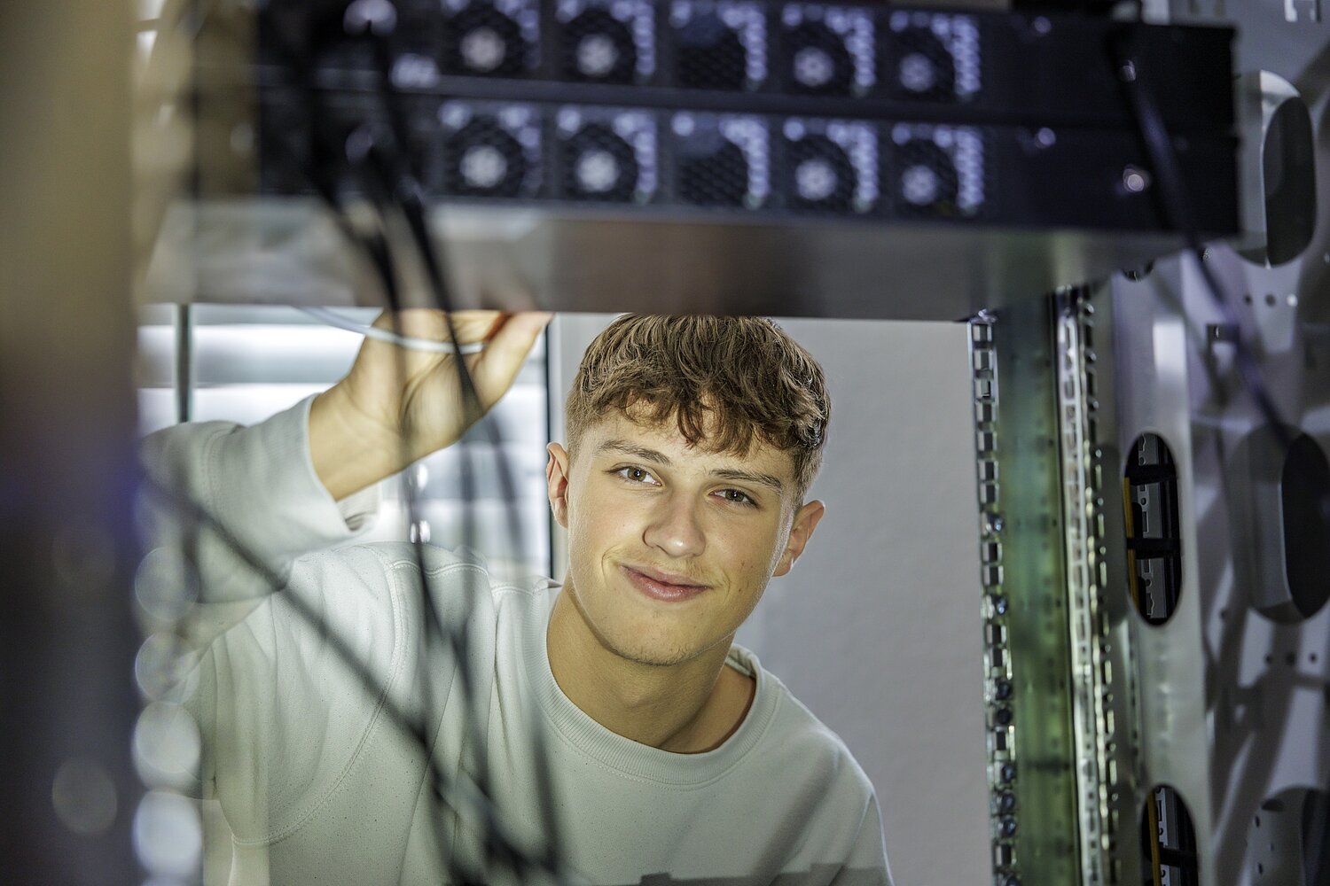 Informatiker, der durch den Serverschrank schaut und in die Kamera blickt.